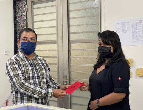Reward presentation: a lab member wearing a face mask and black jacket receives a red envelope.