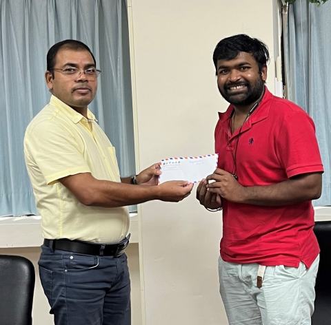 Reward presentation in the lab office: a lab member in a red shirt receives an envelope.
