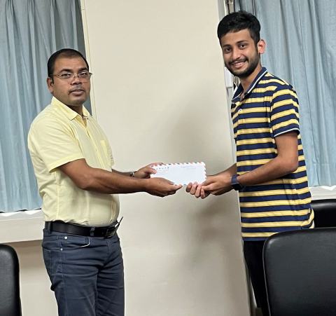 Reward presentation in the lab office: a lab member in a striped shirt receives an envelope.