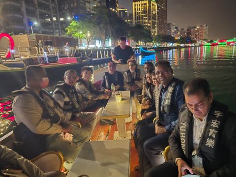 Workshop guests seated in a small boat during an evening river cruise, wearing the boat operator’s vests, with the illuminated skyline behind them.