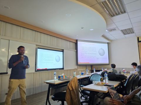 A speaker with a microphone presents a slide on X, Y and Z rotations on the Bloch sphere, shown on two screens, while attendees follow at their desks.