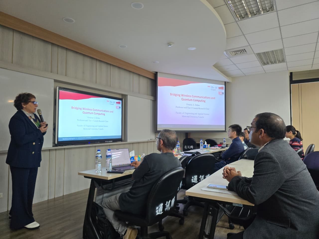 A speaker presents the title slide “Bridging Wireless Communications and Quantum Computing” to workshop attendees in the seminar room.
